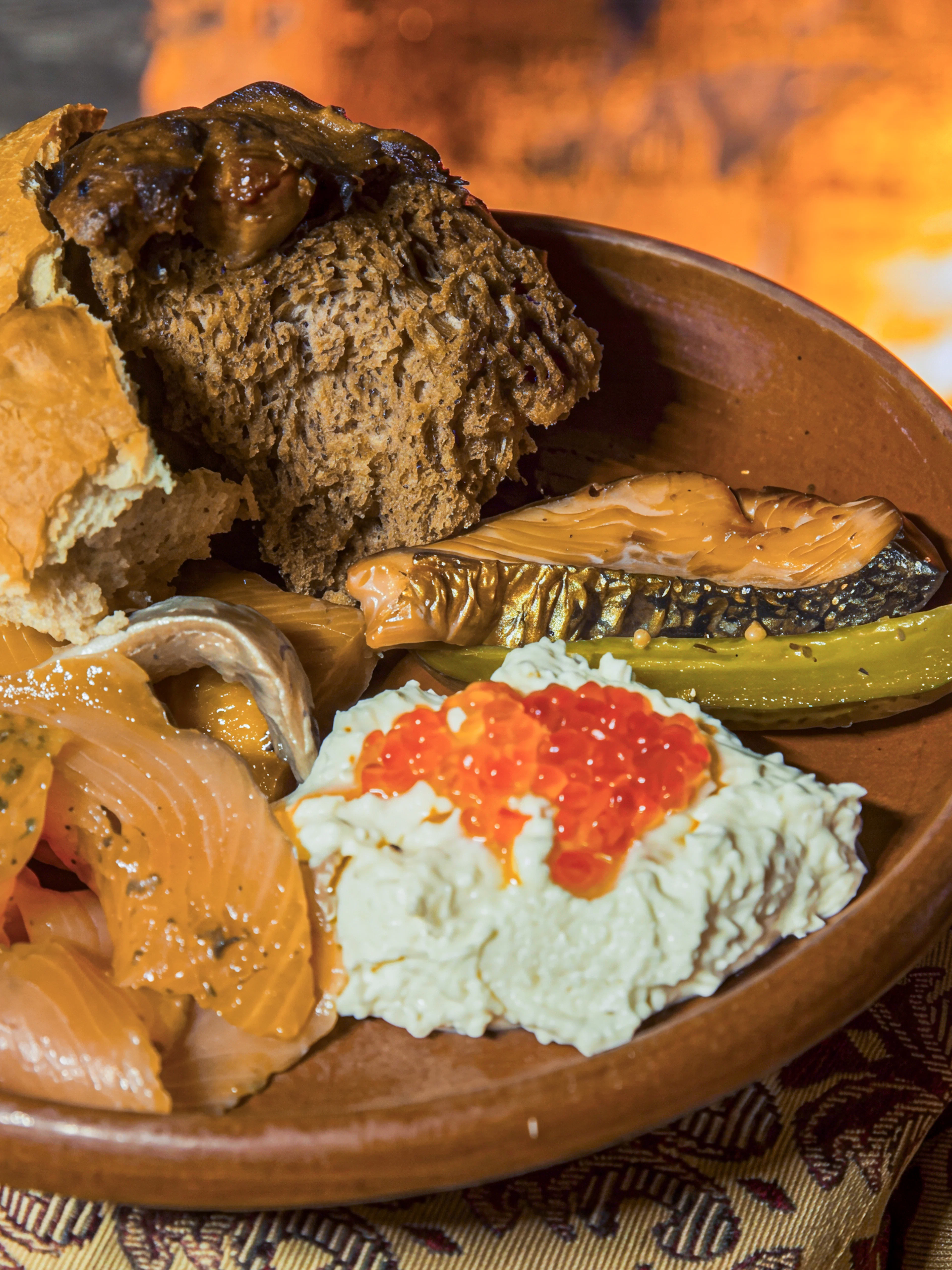 Traditional Estonian meal with smoked fish, eggs, and bread by a fire in Tallinn.