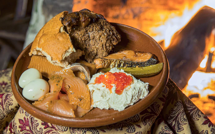 Traditional Estonian meal with smoked fish, eggs, and bread by a fire in Tallinn.