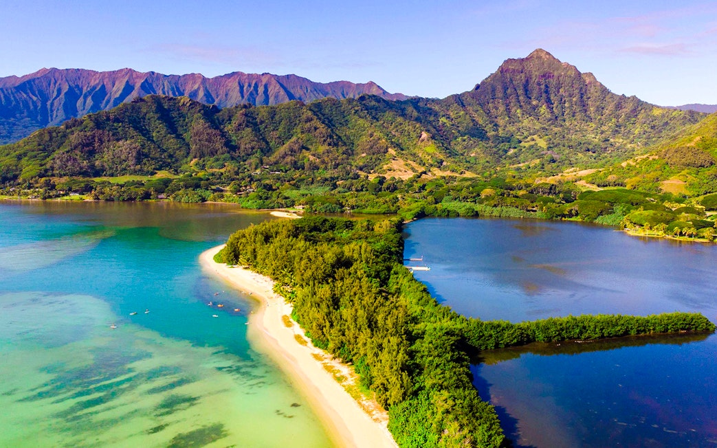 Aerial view of Secret Island and Moli'i Pond in Hawaii with lush greenery and surrounding mountains.