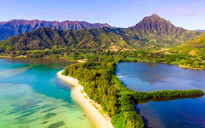 Aerial view of Secret Island and Moli'i Pond in Hawaii with lush greenery and surrounding mountains.