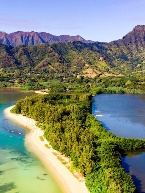 Aerial view of Secret Island and Moli'i Pond in Hawaii with lush greenery and surrounding mountains.