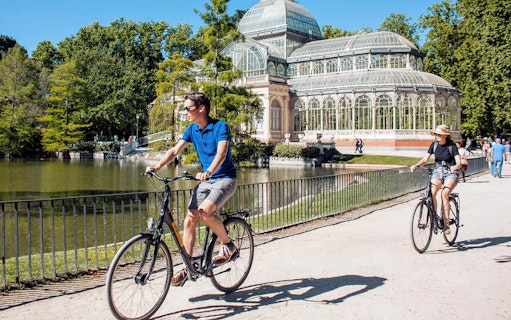 Cyclists riding past the Crystal Palace in Madrid's Retiro Park.