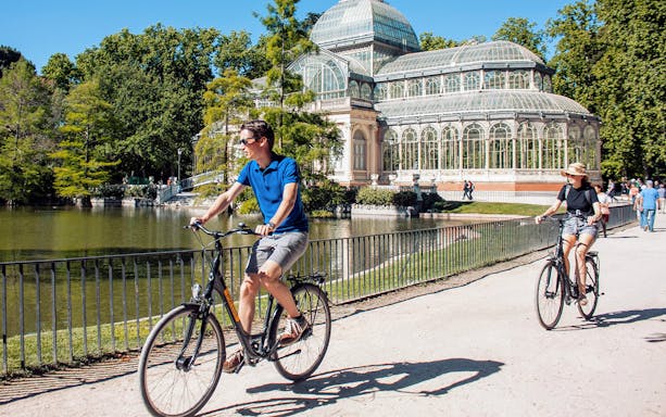 Cyclists riding past the Crystal Palace in Madrid's Retiro Park.
