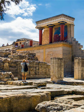 Knossos Palace ruins with red columns on Crete, Greece, visitor exploring site.