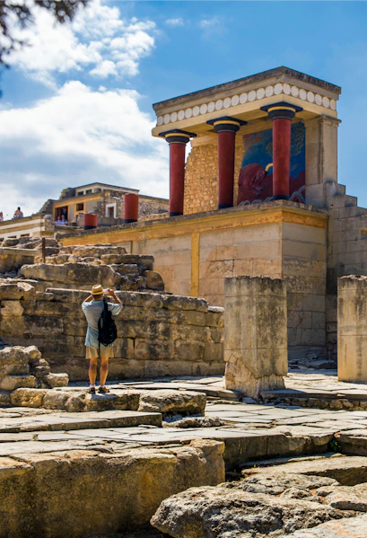 Knossos Palace ruins with red columns on Crete, Greece, visitor exploring site.