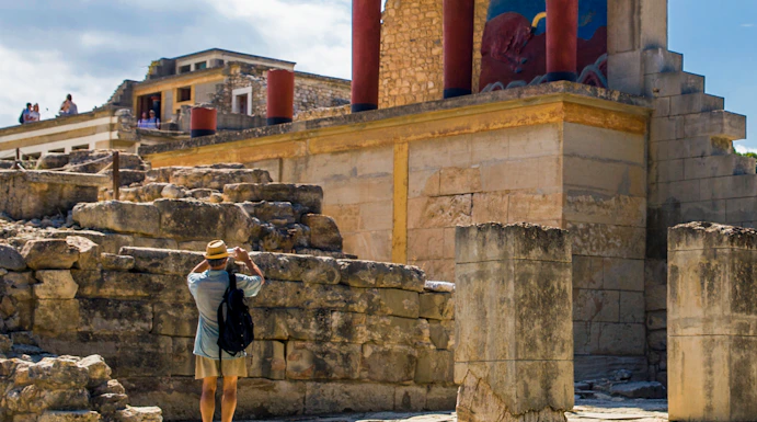 Knossos Palace ruins with red columns on Crete, Greece, visitor exploring site.