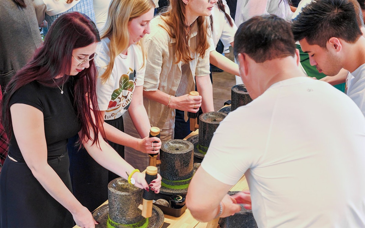 Adults participating in a matcha making class using traditional stone mills.
