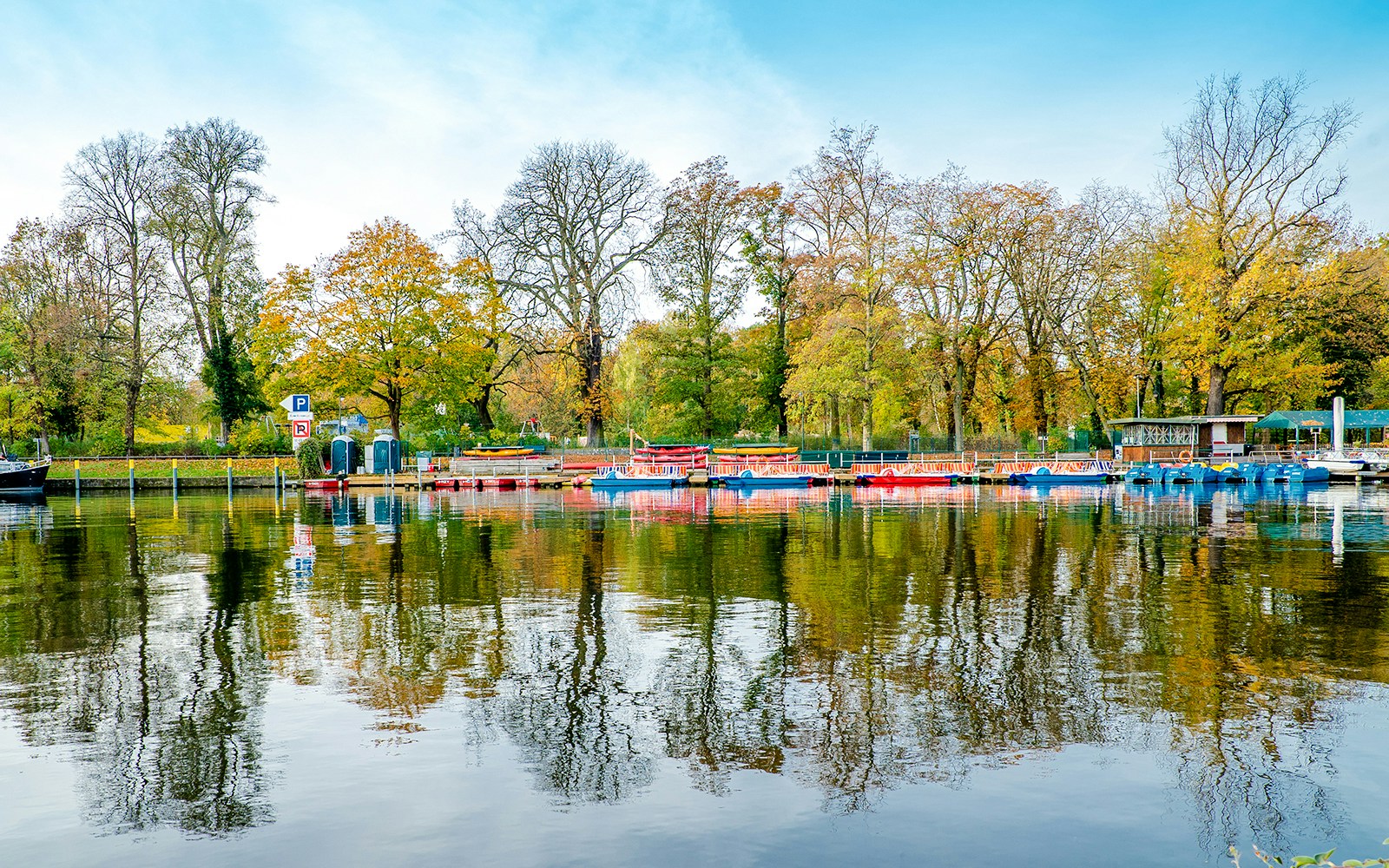 Boats docked at Treptower Park with autumn trees reflected in the water, East Berlin.