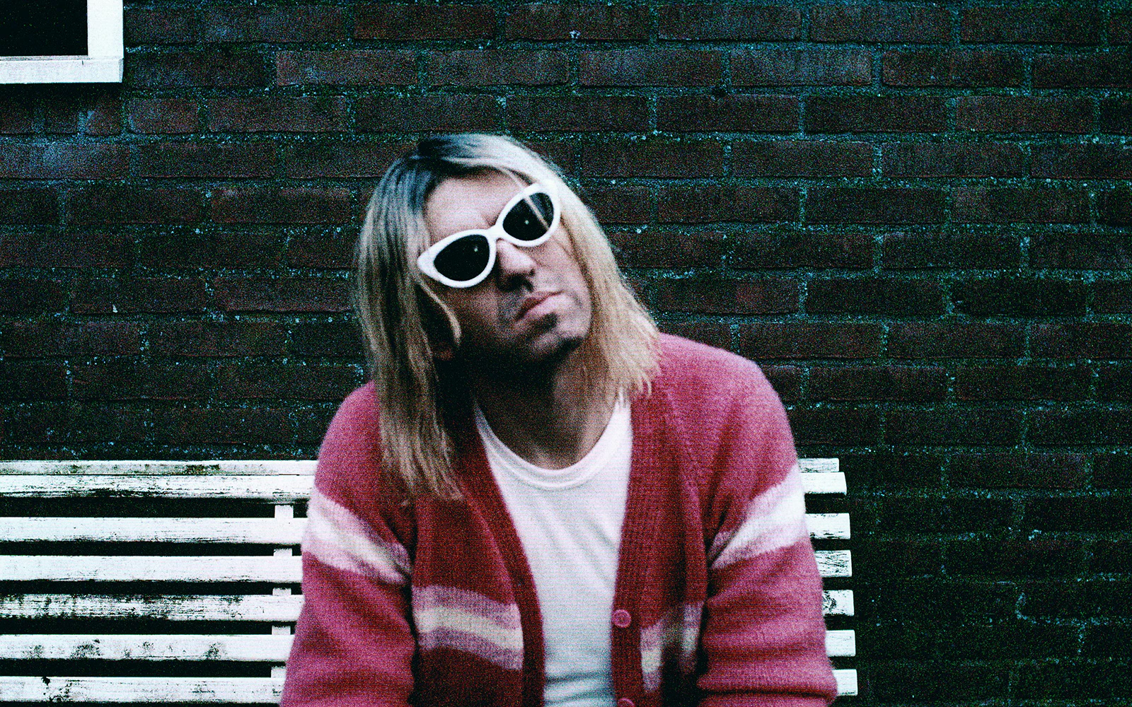 Person in sunglasses and pink sweater sitting on a bench, Anton Corbijn exhibit, Fotografiska Berlin.