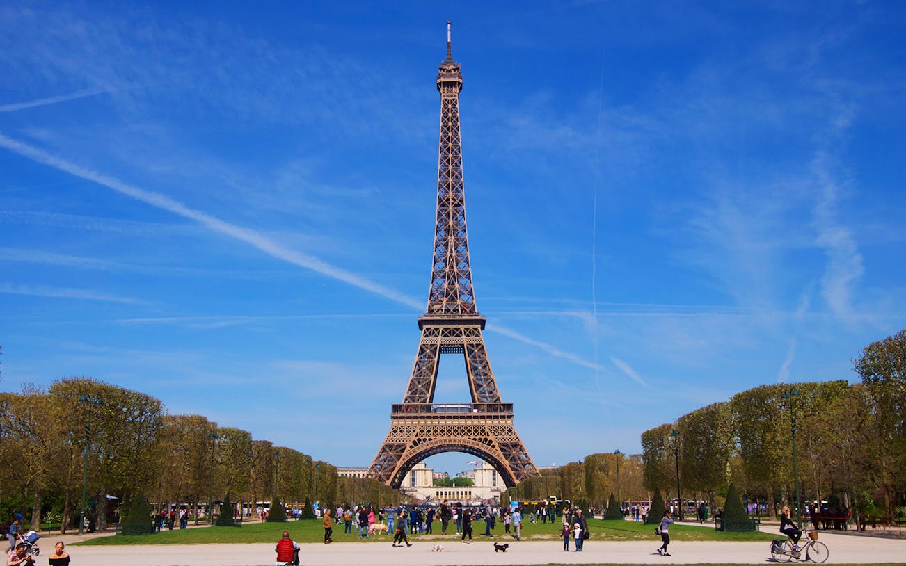 Eiffel Tower in Paris with people walking in the Champ de Mars park.
