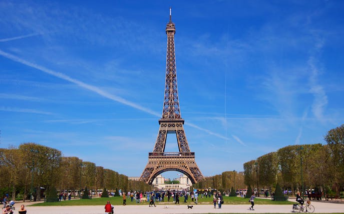 Eiffel Tower in Paris with people walking in the Champ de Mars park.
