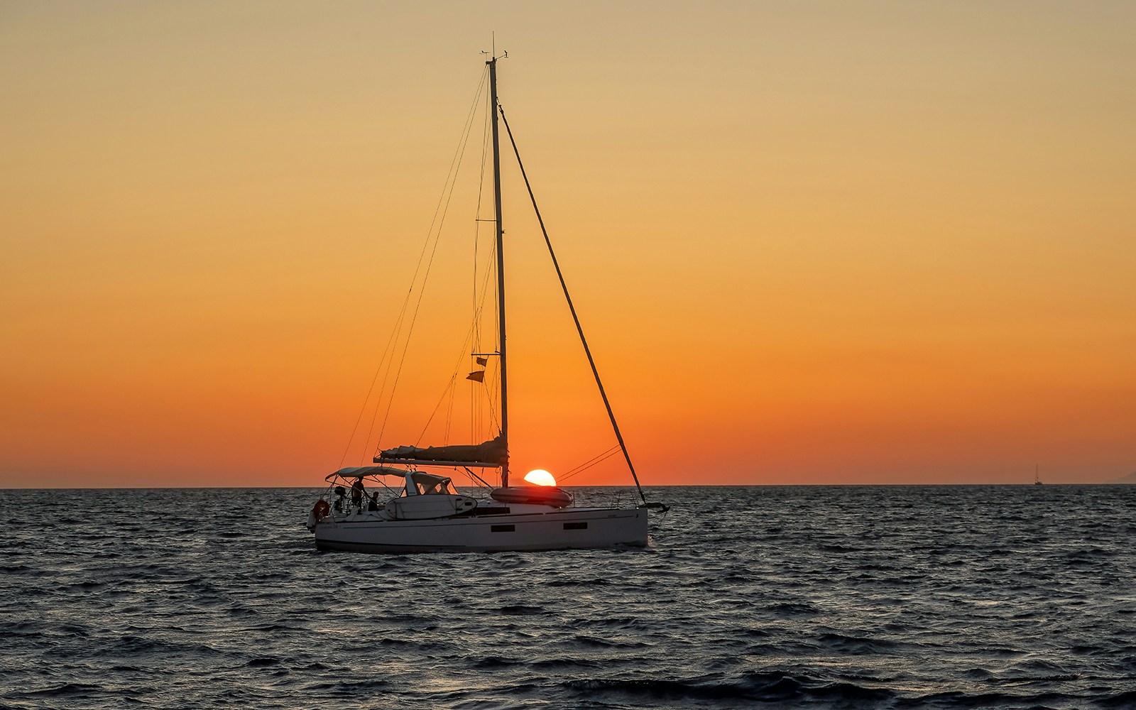 Santorini sunset cruise with sailboat on Aegean Sea, view of caldera cliffs.