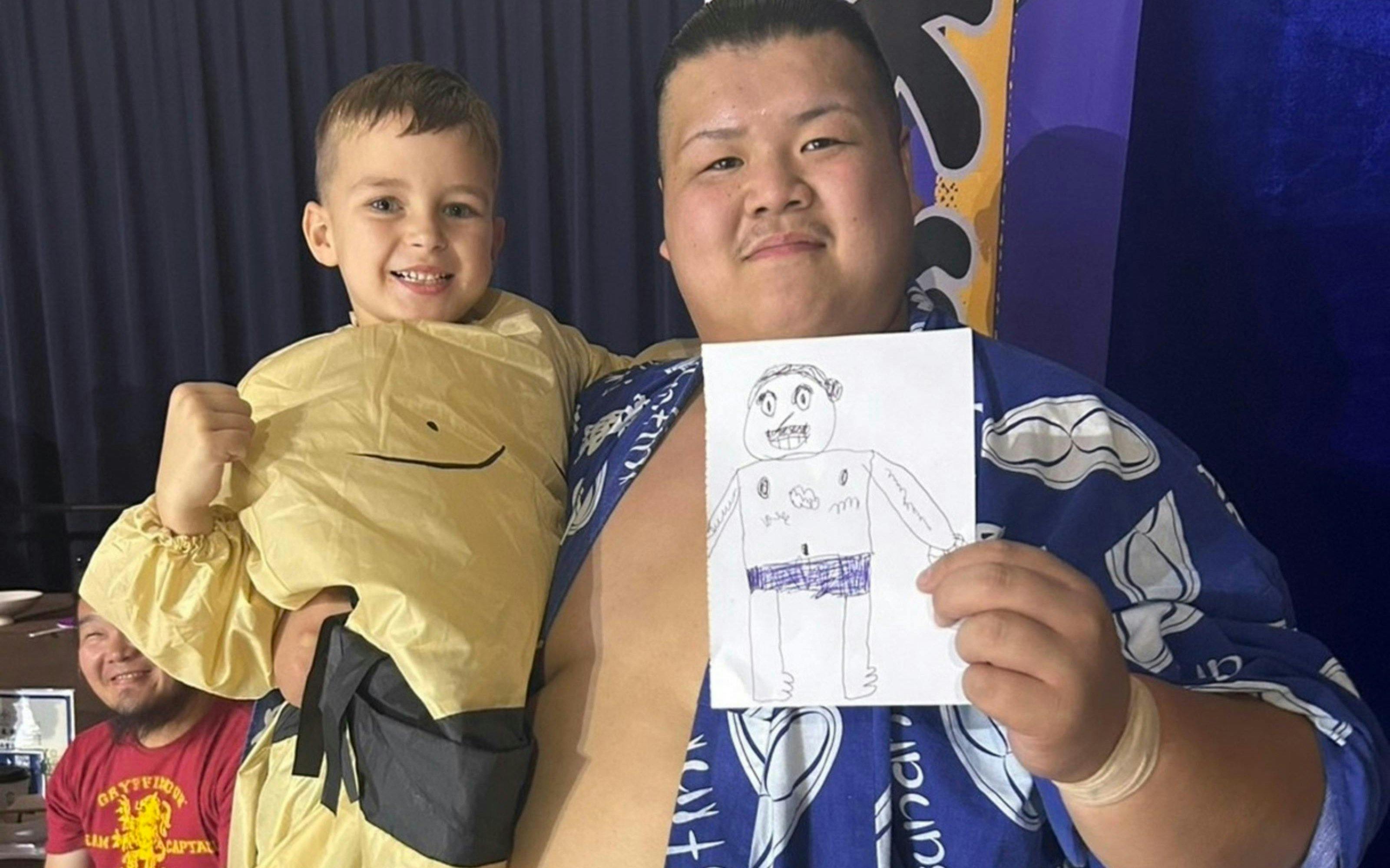 Sumo wrestler and child at Ochiizumibeya holding a drawing during Sumo Practice Show.