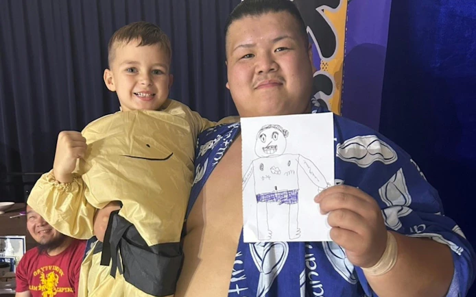 Sumo wrestler and child at Ochiizumibeya holding a drawing during Sumo Practice Show.