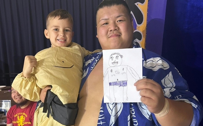 Sumo wrestler and child at Ochiizumibeya holding a drawing during Sumo Practice Show.