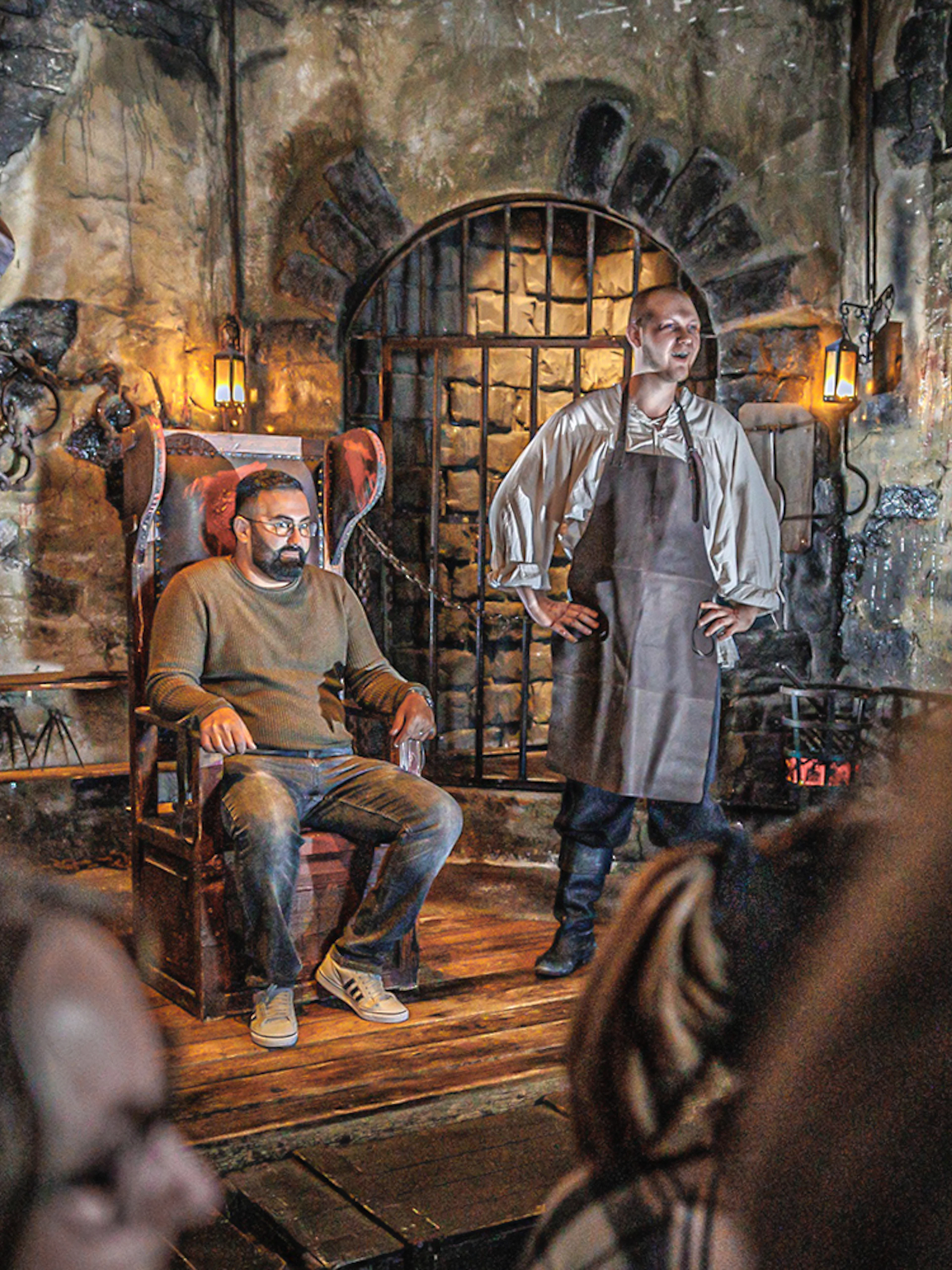 Torturer performing in Hamburg Dungeon with a visitor seated in a medieval setting.