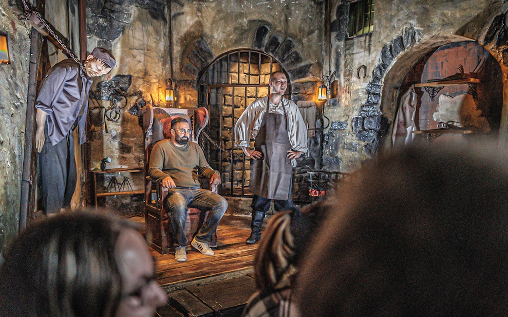 Torturer performing in Hamburg Dungeon with a visitor seated in a medieval setting.