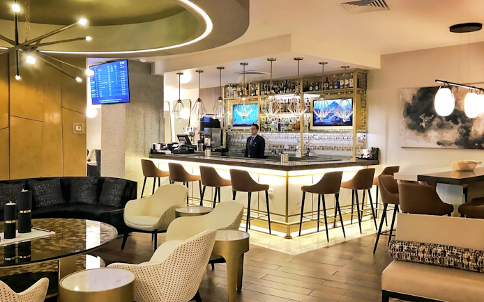 Bar counter at MERA Business Lounge, Cancun Airport, with seating and modern decor.