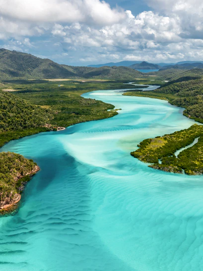 Aerial view of turquoise river winding through lush landscape in Whitsunday Islands, Australia.