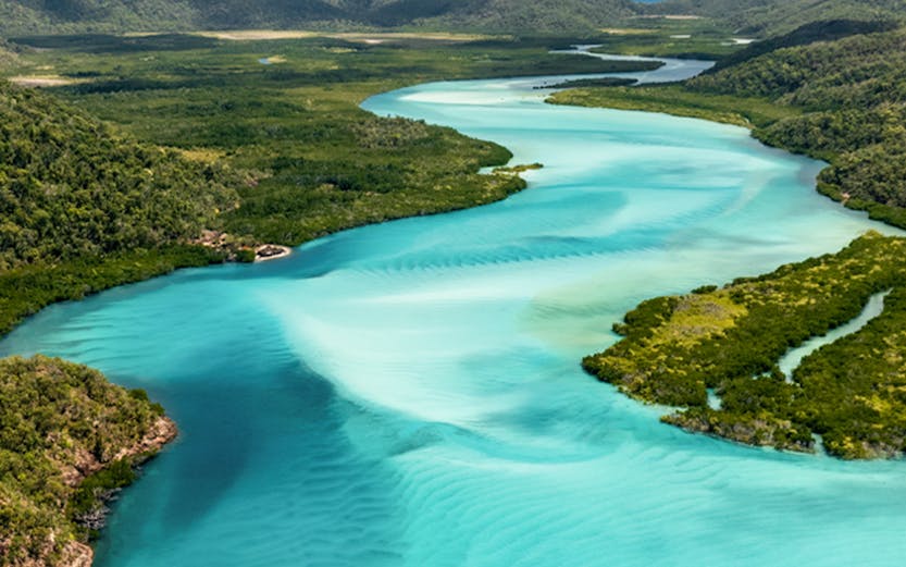 Aerial view of turquoise river winding through lush landscape in Whitsunday Islands, Australia.
