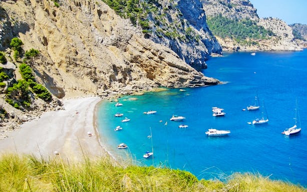 Boats anchored near rocky cliffs and beach at Cala Figuera, Cap Formentor, Mallorca.