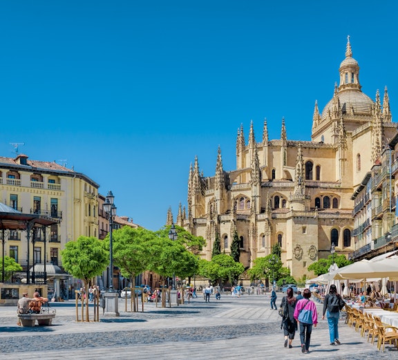 Plaza Mayor in Segovia with Segovia Cathedral in the background, people walking and dining outdoors.