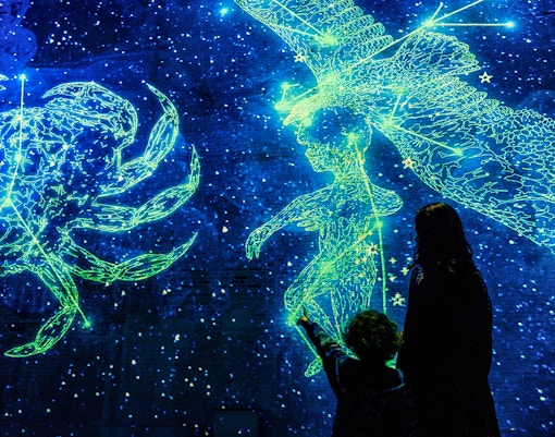 Visitors viewing cosmic light projections at Fabrique des Lumières exhibit.