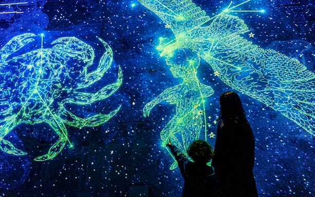 Visitors viewing cosmic light projections at Fabrique des Lumières exhibit.