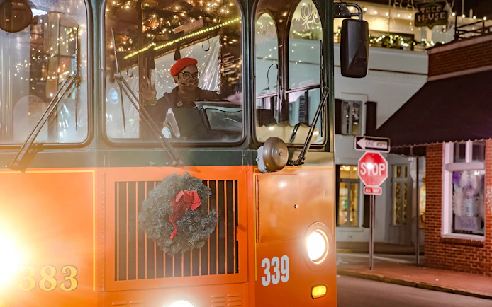 Old Town Trolley decorated with holiday lights and wreath in Savannah at night.