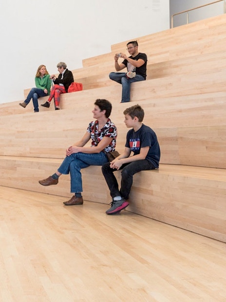 Visitors sitting on wooden steps inside San Francisco Museum of Modern Art.