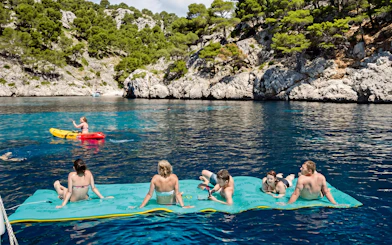 Tourists relaxing on a floating mat and kayaking near a catamaran at Portals Vells.