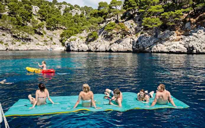Tourists relaxing on a floating mat and kayaking near a catamaran at Portals Vells.