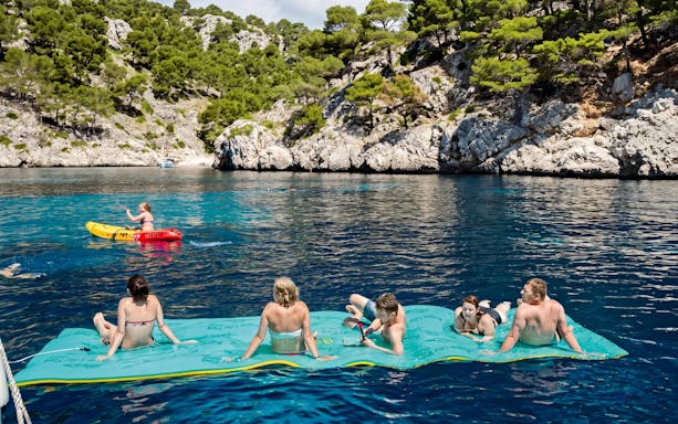 Tourists relaxing on a floating mat and kayaking near a catamaran at Portals Vells.