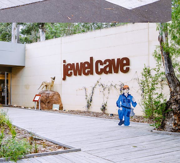 Jewel Cave entrance in Margaret River, featuring a cave explorer cutout and surrounding greenery.