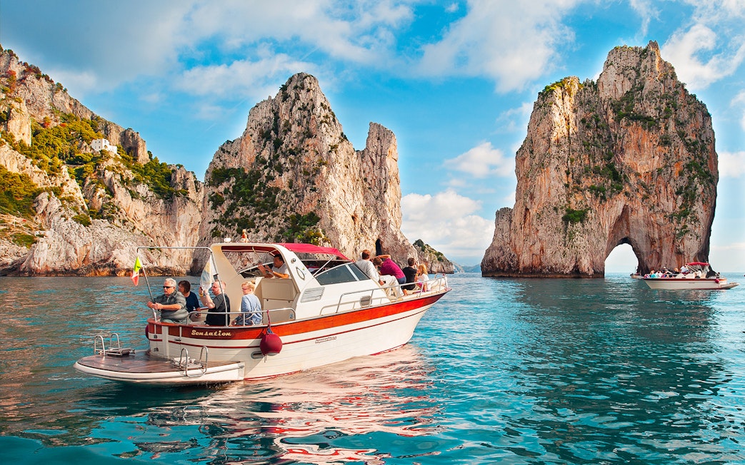 Boat tour near Faraglioni rock formations, Capri, Italy.