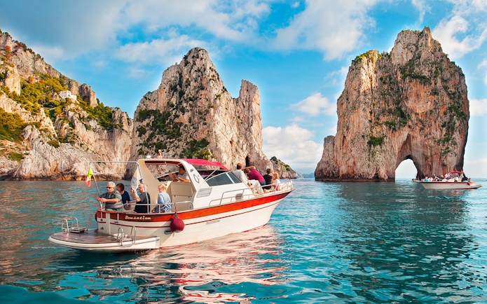 Boat tour near Faraglioni rock formations, Capri, Italy.