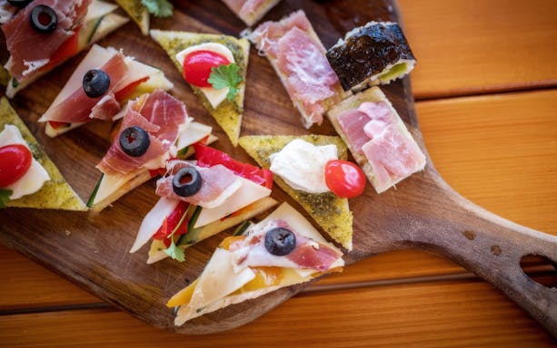 Platter of bite-sized canapés with cured meats, cheese, olives, and cherry tomatoes.