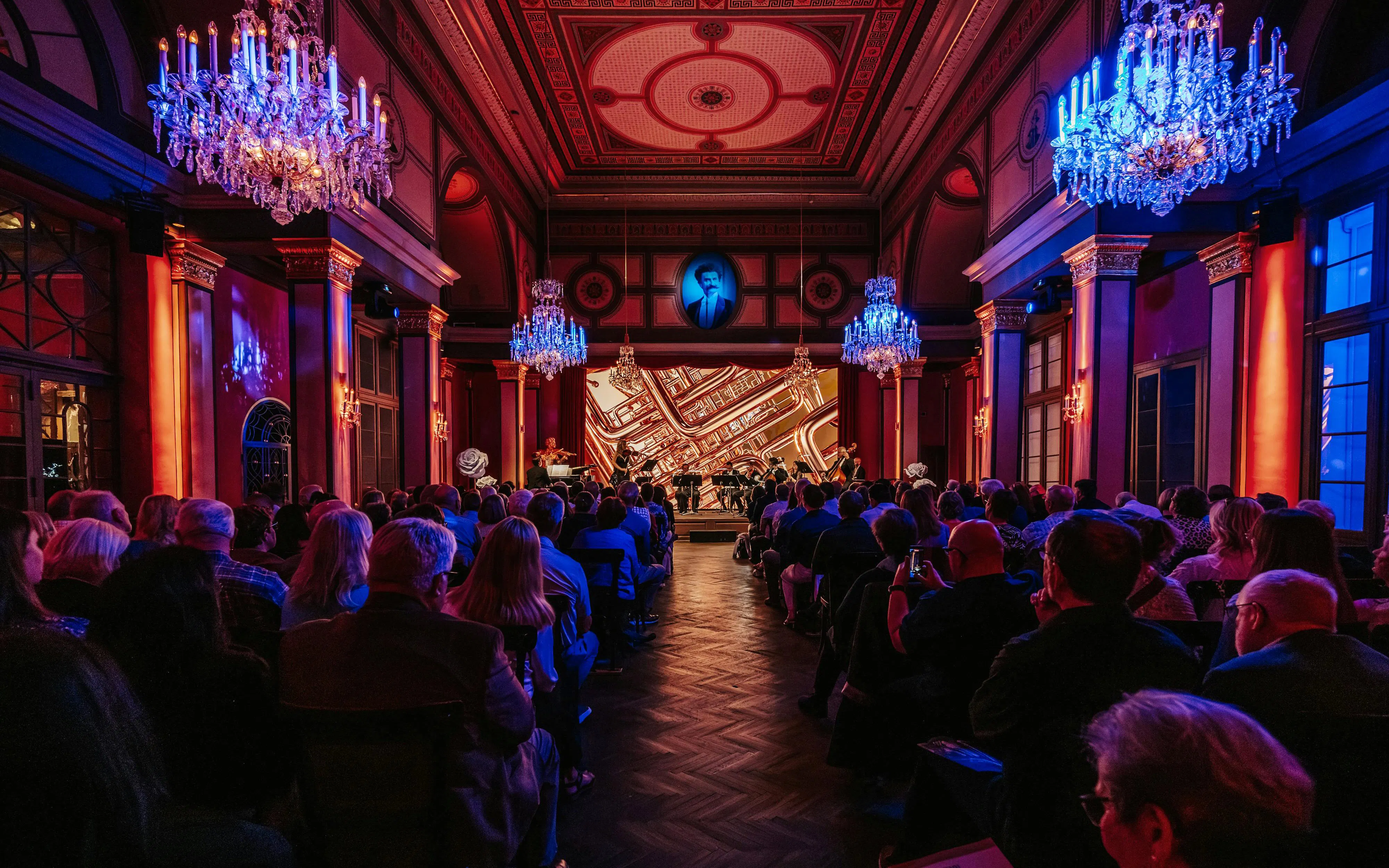 Audience attending a classical concert in a Vienna concert hall with chandeliers.