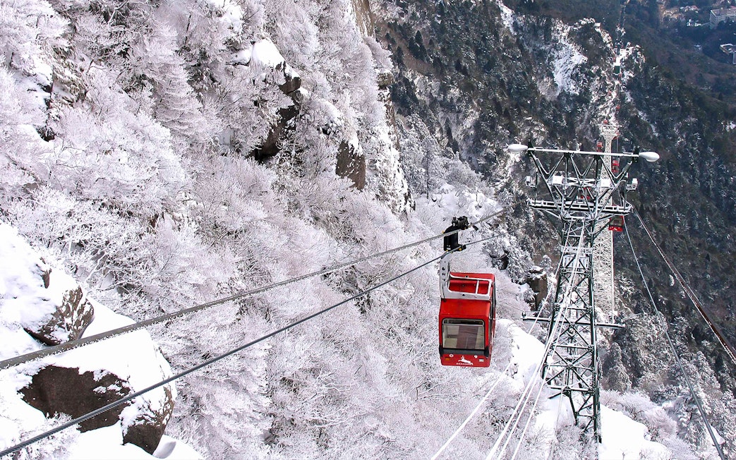 Red cable car ascending snowy mountain with Kintetsu Rail Pass.