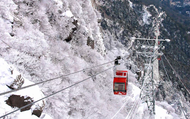 Red cable car ascending snowy mountain with Kintetsu Rail Pass.