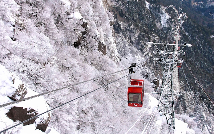 Red cable car ascending snowy mountain with Kintetsu Rail Pass.