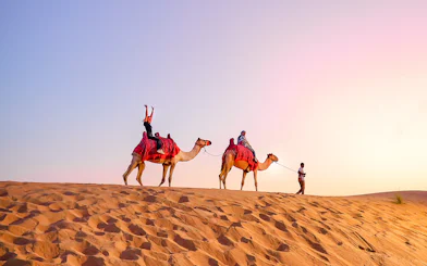 Camel ride during evening desert safari with tourists in the sand dunes.