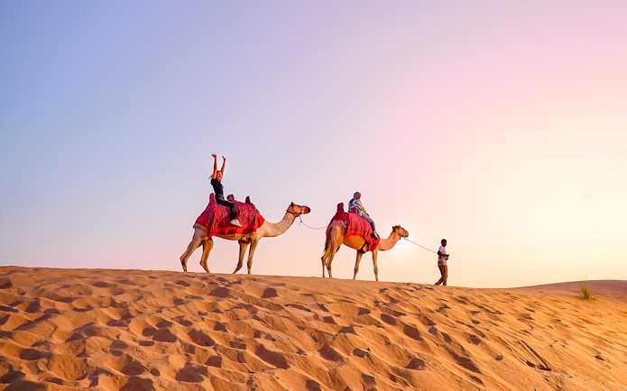 Camel ride during evening desert safari with tourists in the sand dunes.