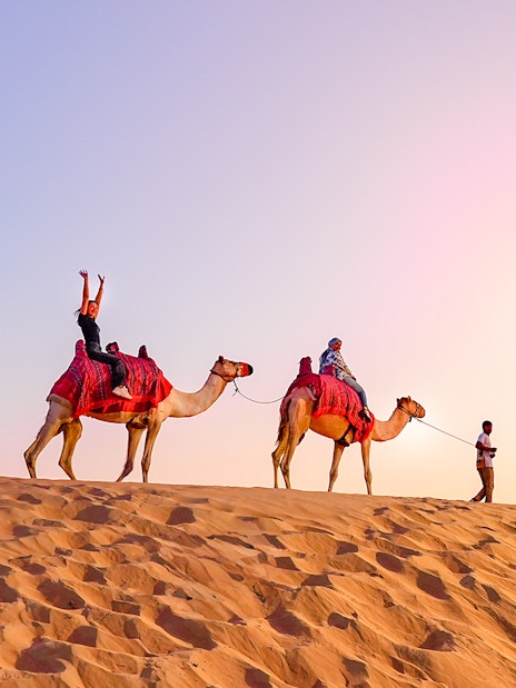 Camel ride during evening desert safari with tourists in the sand dunes.