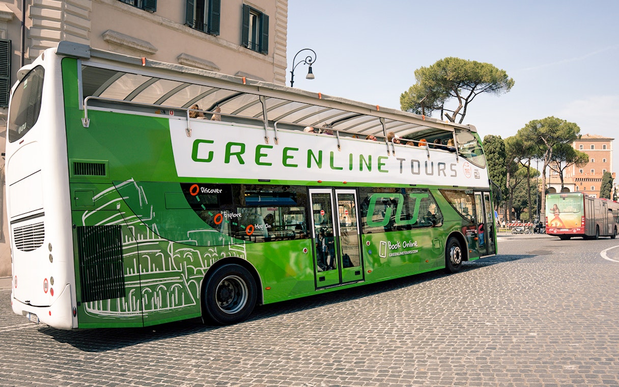 Green Line hop-on hop-off bus in Rome near historic buildings and trees.