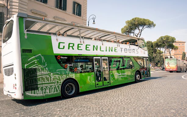 Green Line hop-on hop-off bus in Rome near historic buildings and trees.