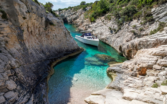 Boat navigating turquoise waters between rocky cliffs at Secret Beach, Vis.