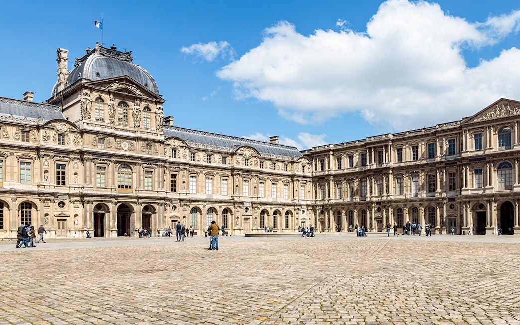Cour Carrée courtyard at Louvre Museum, Paris, with visitors exploring the historic architecture.