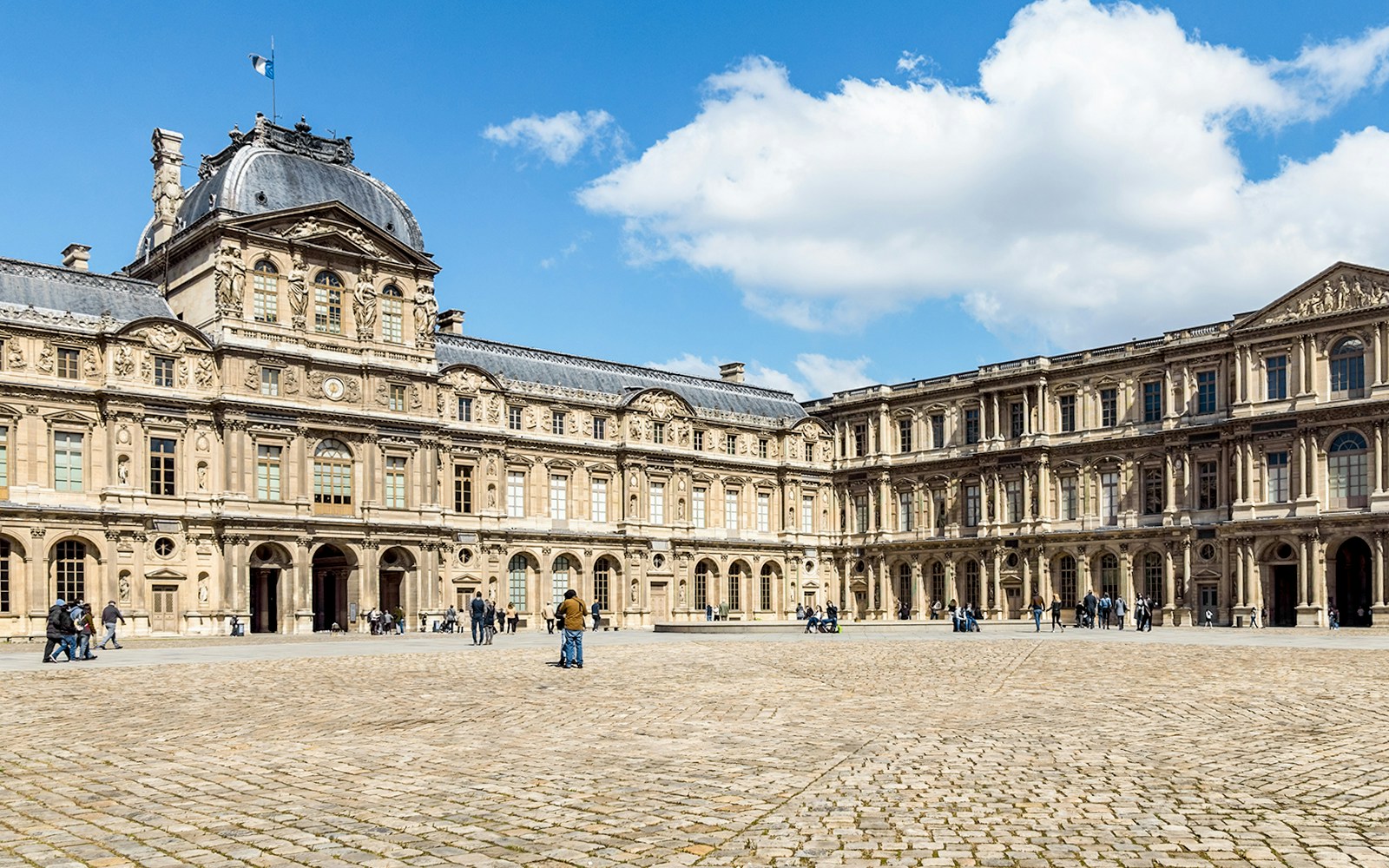 Cour Carrée courtyard at Louvre Museum, Paris, with visitors exploring the historic architecture.