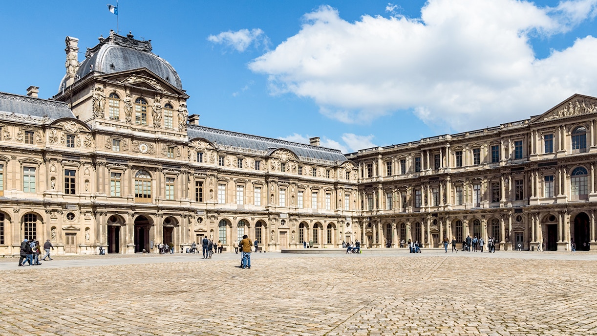 Cour Carrée courtyard at Louvre Museum, Paris, with visitors exploring the historic architecture.